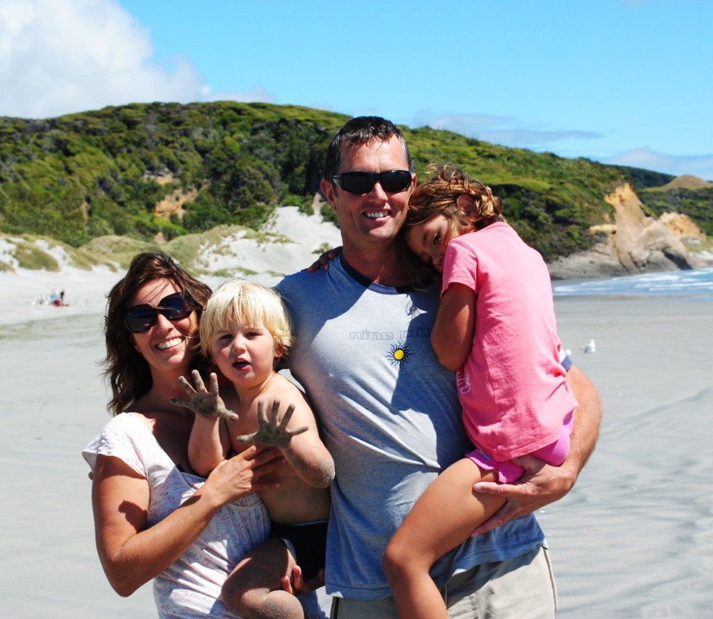 Happy family enjoying a sunny day at the beach with children playing in the sand and scenic cliffs in the background.