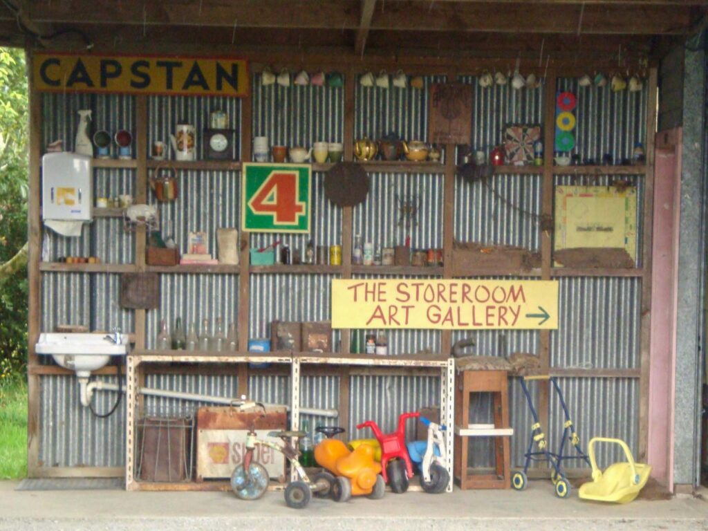 Wall display inside the Storeroom Art Gallery at Langford Store, featuring old toys, kitchenware, retro signs, and rustic collectibles.