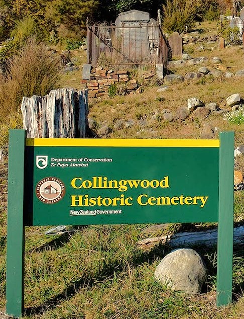 Green and yellow Department of Conservation sign for Collingwood Historic Cemetery with old graves visible in the background.