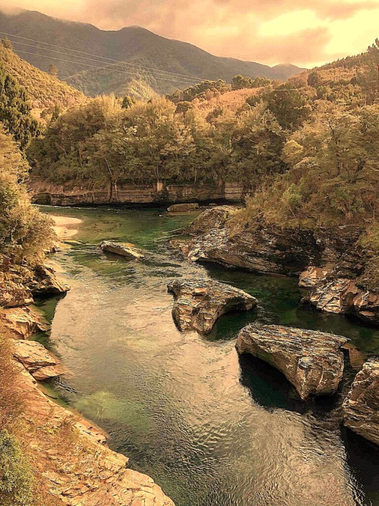 Scenic view of the Aorere River flowing past large rock formations with forested hills and mountains in the background at Salisbury Falls, Golden Bay.