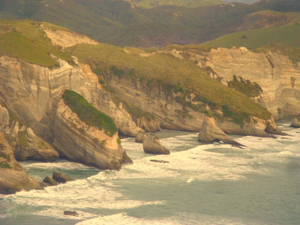 Sandstone cliffs with green vegetation and crashing waves at Wharariki Beach, Golden Bay, New Zealand.