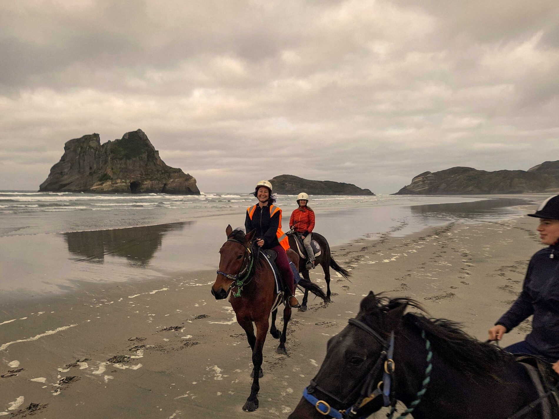 Horseback riders enjoying a scenic trek along Wharariki Beach with rocky sea stacks in the background, with North West Horse Treks, near Station House Motel in Golden Bay, New Zealand.