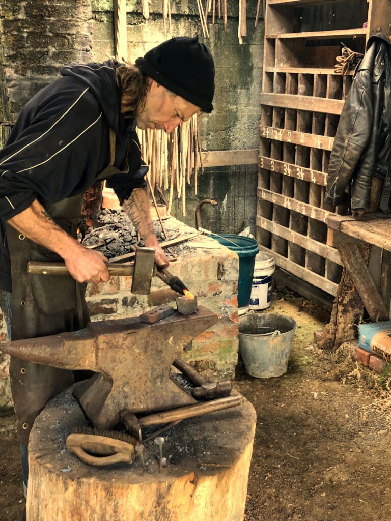 Traditional blacksmith workshop in New Zealand with forge, anvil, and hand tools, featuring a blacksmith demonstrating techniques to visitors.