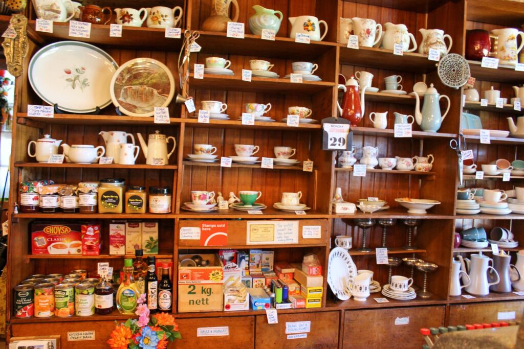 Vintage wooden shelves inside The Langford Store in Bainham, New Zealand, displaying antique teacups, teapots, kitchenware, and pantry goods.