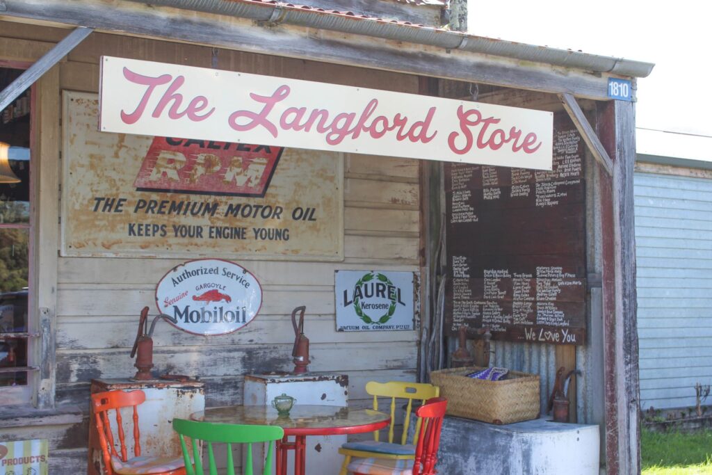 Historic Langford Store in Bainham, New Zealand, featuring vintage petrol signs, rustic wooden exterior, and colorful outdoor chairs.